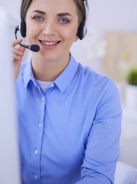 Ofisinde kulaklık takmış, telefon operatörü olarak çalışan ciddi ve güzel bir genç kadın.