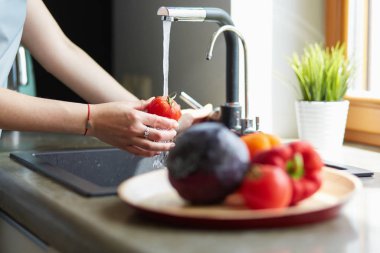 Mutfak lavabosunda domates yıkayan bir kadın.
