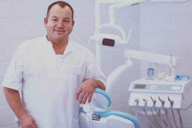 Diş kliniğinde duran gülümseyen bir dişçinin portresi.