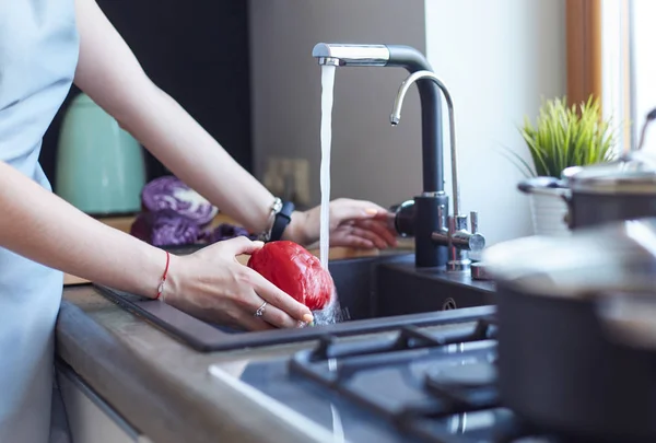 Een vrouw die groenten wast. mooie jonge vrouw wassen groenten voor salade en glimlachen terwijl staan in de keuken — Stockfoto