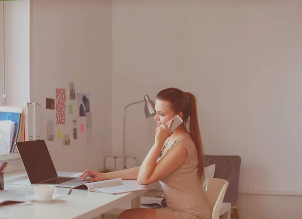 Jolie femme assise au bureau, travaillant avec un ordinateur portable, tenant un document — Photo