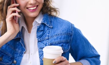 Kafede kahve içip cep telefonuyla konuşan genç bir kadın.