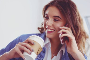 Kafede kahve içip cep telefonuyla konuşan genç bir kadın.