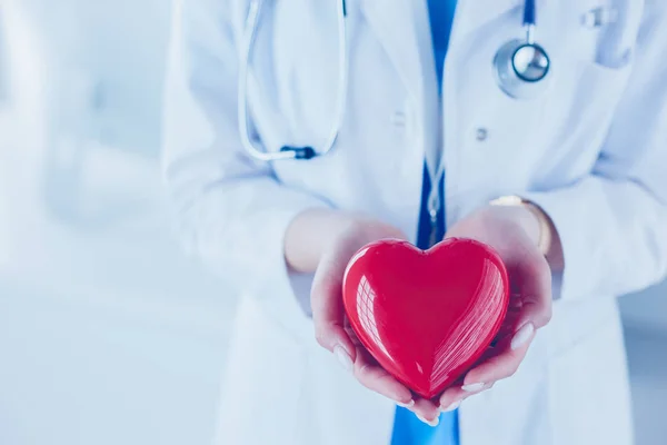 Doctora con estetoscopio sosteniendo el corazón, sobre fondo claro — Foto de Stock