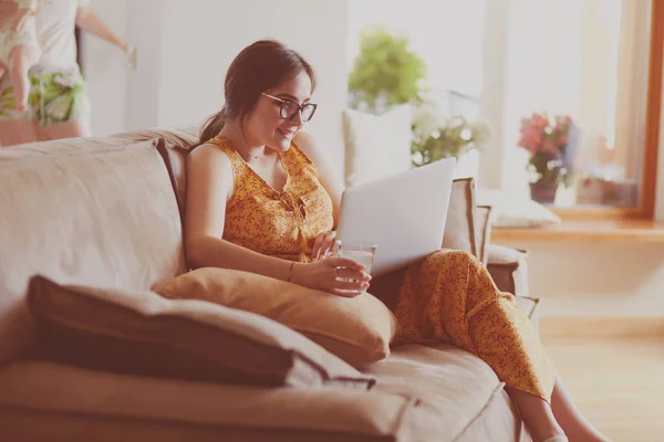 Mujer joven sentada en el sofá trabajando en el ordenador portátil en casa —  Fotos de Stock