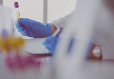 Kadın araştırmacı, beyaz arka planda izole edilmiş ilaç şişeleri ve mataralarla çevrili.