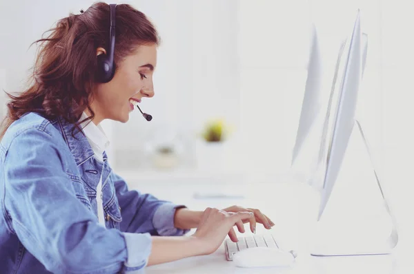 Glad charmig ung kvinna sitter och arbetar med bärbar dator med headset på kontoret — Stockfoto