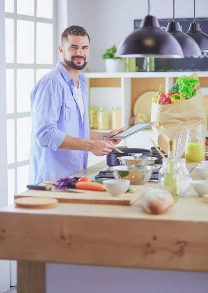 Man following recipe on digital tablet and cooking tasty and healthy food in kitchen at home — Stock Photo, Image