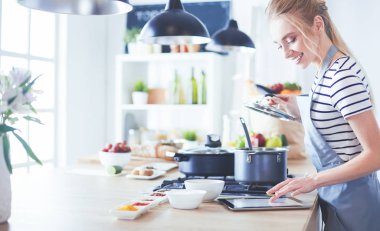 Mutfakta yemek yapmak için tablet bilgisayar kullanan genç bir kadın.