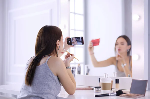 Blogger de belleza filmando tutorial de maquillaje con teléfono inteligente frente al espejo —  Fotos de Stock