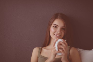 Bir fincan çay ya da kahveyle yerde oturmuş gülümseyen sağlıklı bir genç.