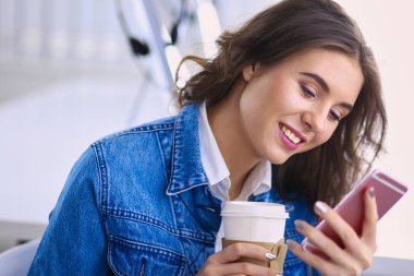 Kafede kahve içip cep telefonuyla konuşan genç bir kadın.