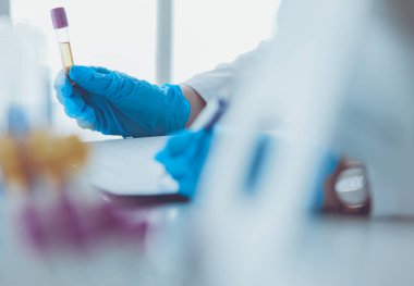 Kadın araştırmacı, beyaz arka planda izole edilmiş ilaç şişeleri ve mataralarla çevrili.