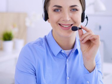 Ofisinde kulaklık takmış, telefon operatörü olarak çalışan ciddi ve güzel bir genç kadın.