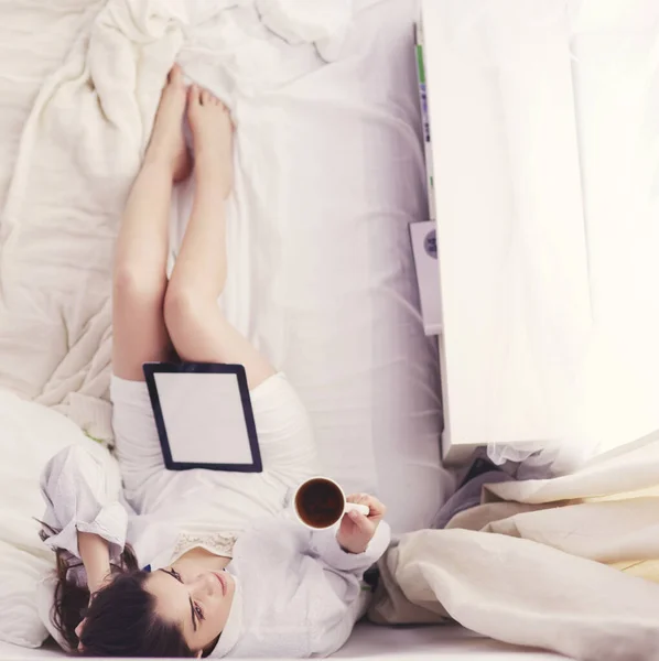 Retrato de la mujer usando tableta y tomando café mientras está sentada en la cama por la mañana —  Fotos de Stock