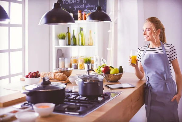 Attraktiv kvinna som håller ett glas apelsinjuice stående i köket — Stockfoto