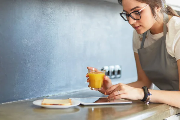 Atraktivní žena drží sklenici pomerančového džusu, zatímco stojí v kuchyni — Stock fotografie