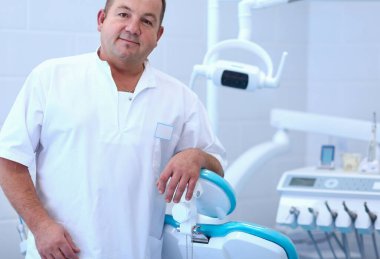 Diş kliniğinde duran gülümseyen bir dişçinin portresi.