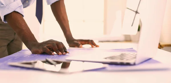 Afrikansk amerikansk arkitekt arbejder med computer og tegninger på kontoret - Stock-foto