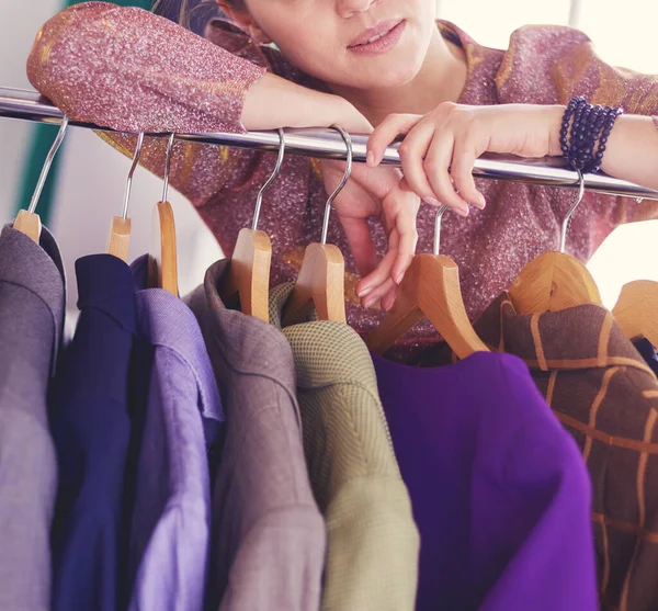 Schöne junge Stylistin in der Nähe von Gestell mit Kleiderbügeln — Stockfoto