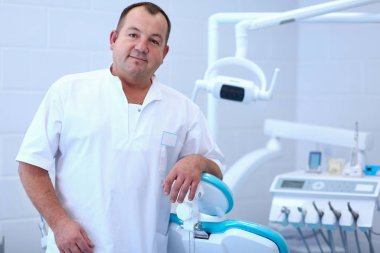 Diş kliniğinde duran gülümseyen bir dişçinin portresi.