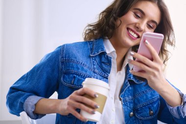 Kafede kahve içip cep telefonuyla konuşan genç bir kadın.