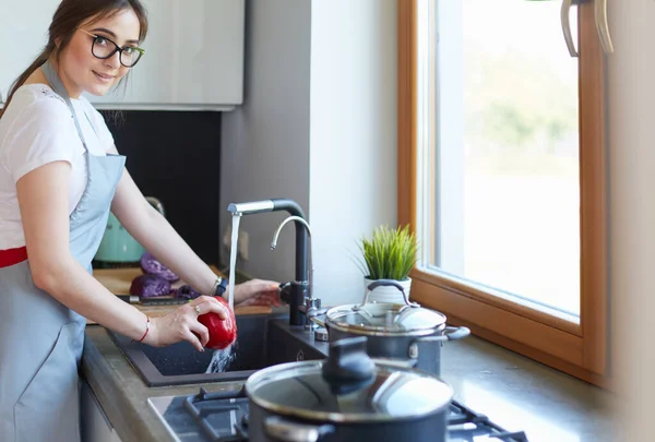 Een vrouw die groenten wast. mooie jonge vrouw wassen groenten voor salade en glimlachen terwijl staan in de keuken — Stockfoto