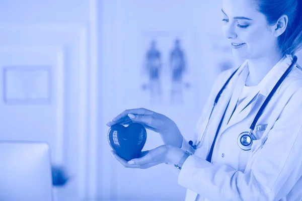 Médica com estetoscópio segurando coração, em fundo claro — Fotografia de Stock