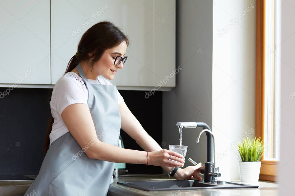 Human hand holding glass pouring fresh drink water at kitchen faucet