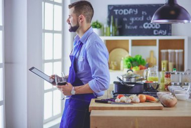 Dijital tablet ve yemek pişirme tarifine uyan bir adam evdeki mutfakta lezzetli ve sağlıklı yemekler pişiriyor.