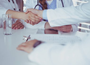 Doktor beyaz arka planda izole edilmiş bir hastayla el sıkışıyor.