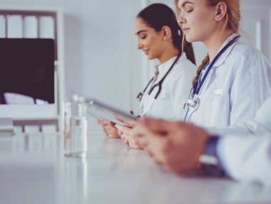 Toplantıdaki doktorlar, masanın üstünde oturuyorlar.