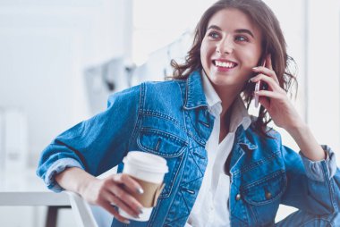 Kafede kahve içip cep telefonuyla konuşan genç bir kadın.