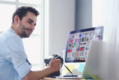 İnternette çalışırken bilgisayarın ve dizüstü bilgisayarın önünde grafik stüdyosunda oturan genç tasarımcının portresi.