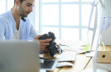 İnternette çalışırken bilgisayarın ve dizüstü bilgisayarın önünde grafik stüdyosunda oturan genç tasarımcının portresi.