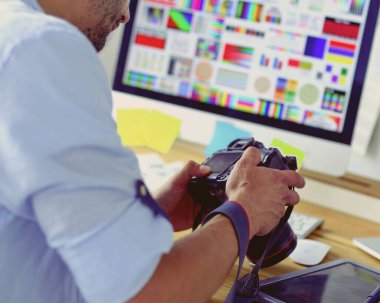 İnternette çalışırken bilgisayarın ve dizüstü bilgisayarın önünde grafik stüdyosunda oturan genç tasarımcının portresi.