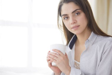 Yatakta oturup kitap okuyan ve kahvaltı yapan bir kadın.