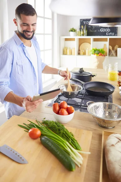 Человек по рецепту на цифровой планшет и приготовление вкусной и здоровой пищи на кухне в домашних условиях — стоковое фото