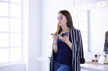 Makyaj fırçası yüzüne yakın bir kadın portresi.