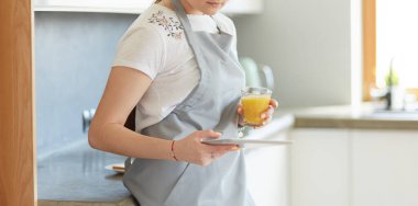 Mutfakta portakal suyu ve tableti olan genç bir kadın.