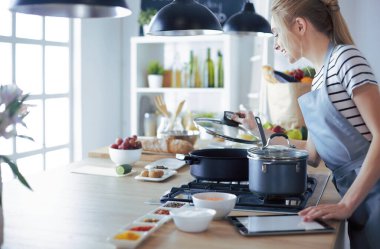 Mutfakta yemek yapmak için tablet bilgisayar kullanan genç bir kadın.