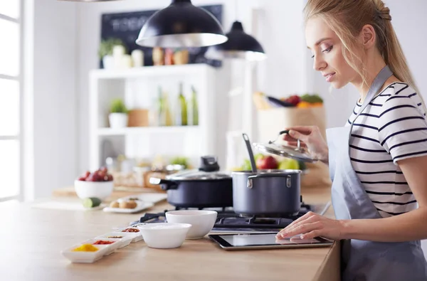 Молода жінка використовує планшетний комп'ютер для приготування їжі на кухні — стокове фото