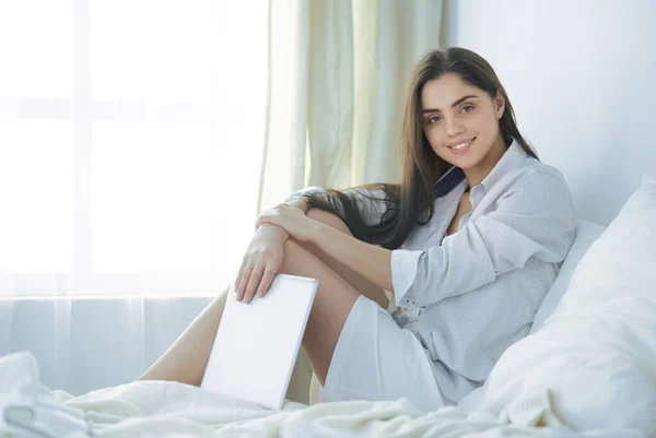 Portret van een vrouw die een tablet gebruikt en 's ochtends koffie drinkt terwijl ze op bed zit — Stockfoto