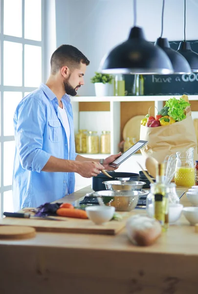 Homem seguindo receita em tablet digital e cozinhar comida saborosa e saudável na cozinha em casa — Fotografia de Stock