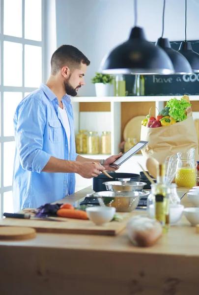 Man following recipe on digital tablet and cooking tasty and healthy food in kitchen at home — Stock Photo, Image