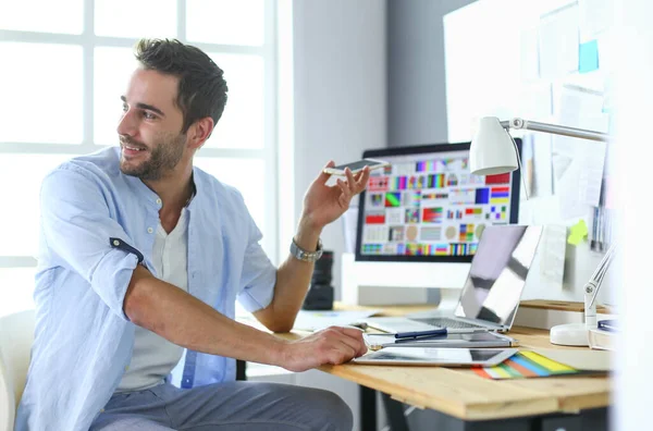 Πορτρέτο του νεαρού σχεδιαστή που κάθεται στο γραφιστικό στούντιο μπροστά από το laptop και τον υπολογιστή ενώ εργάζεται στο διαδίκτυο. — Φωτογραφία Αρχείου