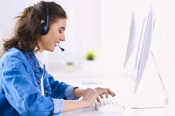 Jovem encantadora feliz sentada e trabalhando com laptop usando fone de ouvido no escritório — Fotografia de Stock