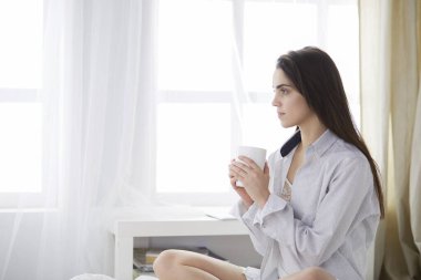 Yatakta oturup kitap okuyan ve kahvaltı yapan bir kadın.