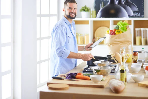 Man following recipe on digital tablet and cooking tasty and healthy food in kitchen at home — Stock Photo, Image