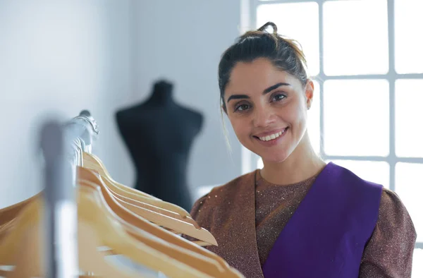 Beautiful young stylist near rack with hangers